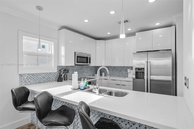 kitchen with a kitchen bar, sink, hanging light fixtures, appliances with stainless steel finishes, and white cabinets