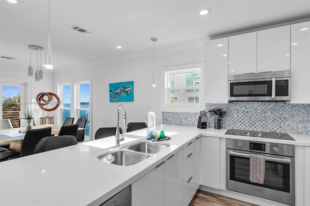 kitchen with sink, hanging light fixtures, kitchen peninsula, stainless steel appliances, and white cabinets