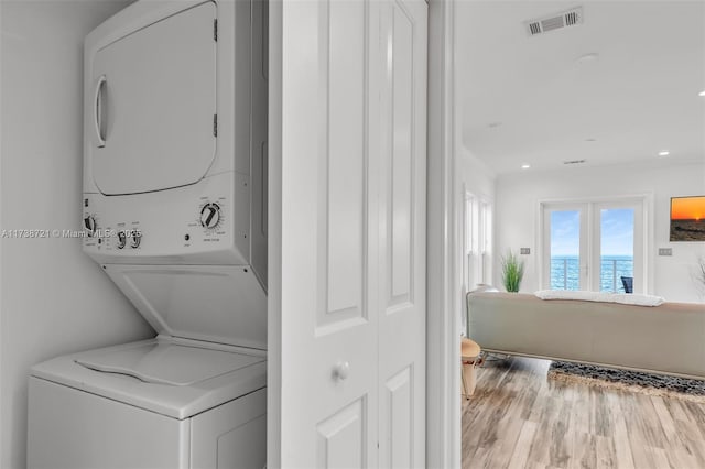 washroom featuring a water view, stacked washer and clothes dryer, and wood-type flooring