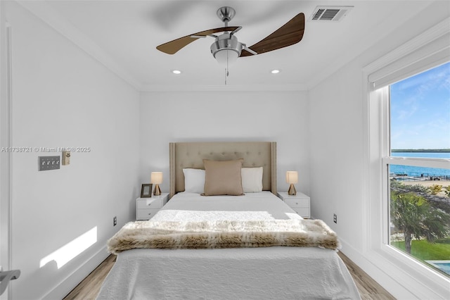 bedroom featuring multiple windows, light wood-type flooring, ceiling fan, and a water view