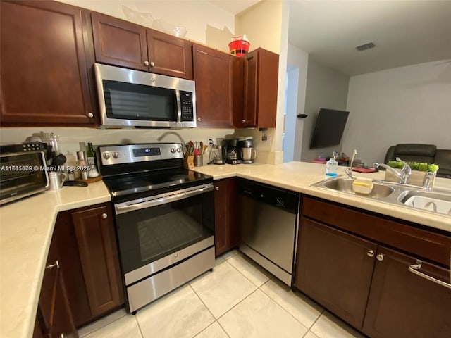 kitchen with sink, kitchen peninsula, appliances with stainless steel finishes, and light tile patterned floors