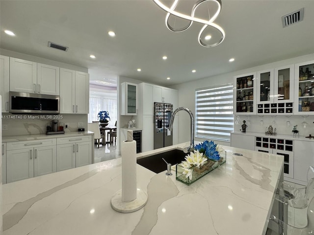 kitchen with a kitchen bar, white cabinetry, black fridge, hanging light fixtures, and light stone countertops