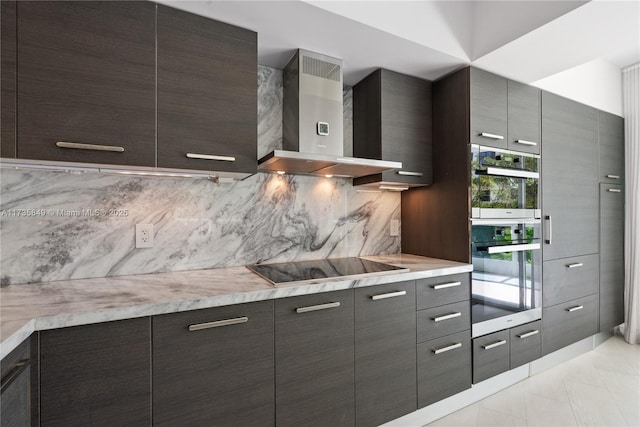 kitchen featuring tasteful backsplash, stainless steel double oven, black electric stovetop, dark brown cabinets, and wall chimney range hood