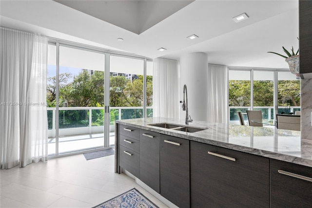 kitchen with dark brown cabinetry, sink, light stone counters, and a wall of windows