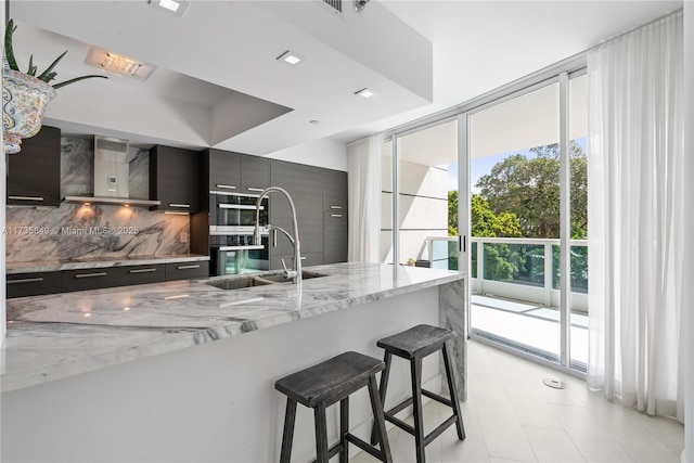 kitchen featuring sink, a breakfast bar area, a wall of windows, light stone countertops, and decorative backsplash