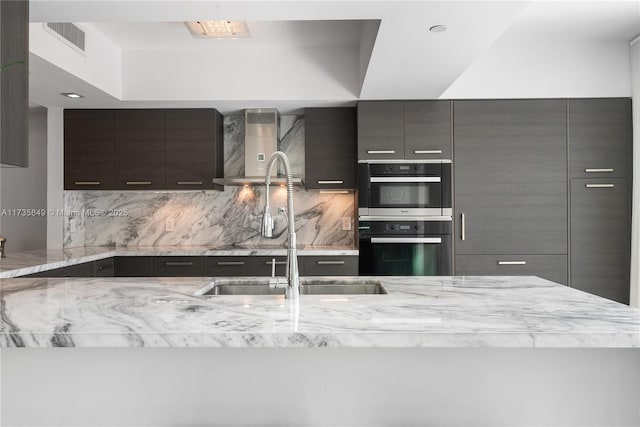 kitchen with double wall oven, sink, backsplash, and wall chimney exhaust hood