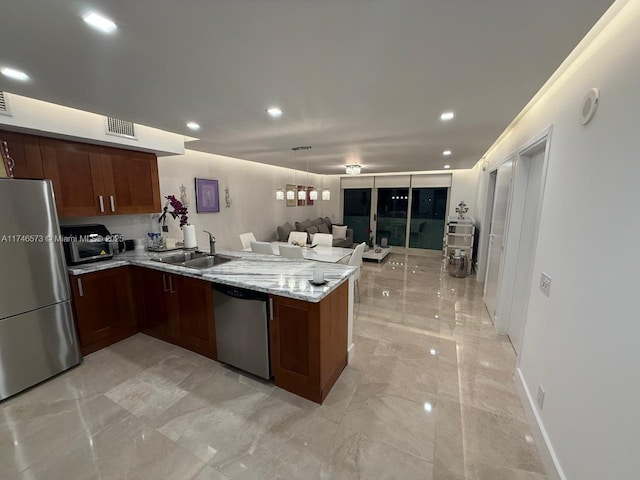 kitchen featuring stainless steel appliances, light stone countertops, sink, and kitchen peninsula