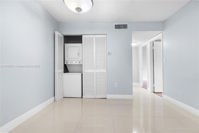 empty room with light tile patterned floors, stacked washer / drying machine, visible vents, a textured ceiling, and baseboards