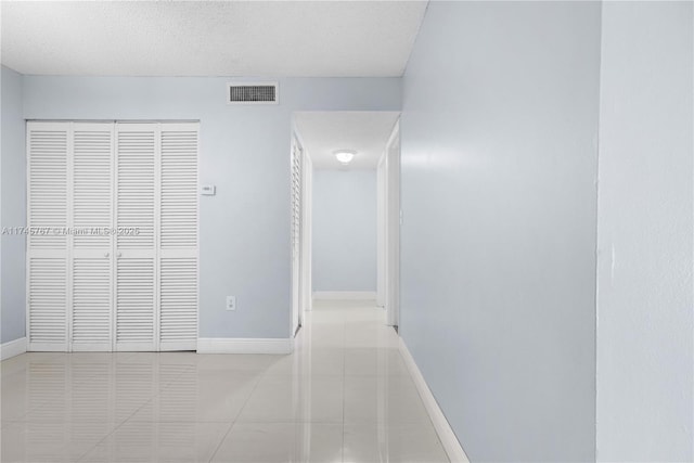 corridor with visible vents, a textured ceiling, baseboards, and tile patterned floors