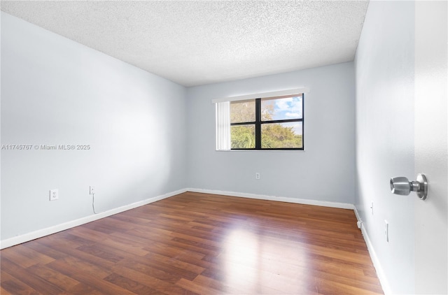 empty room with a textured ceiling, wood finished floors, and baseboards