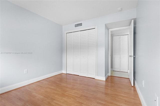 unfurnished bedroom with a closet, baseboards, visible vents, and light wood finished floors