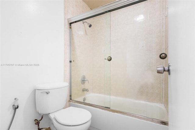 bathroom featuring toilet and bath / shower combo with glass door