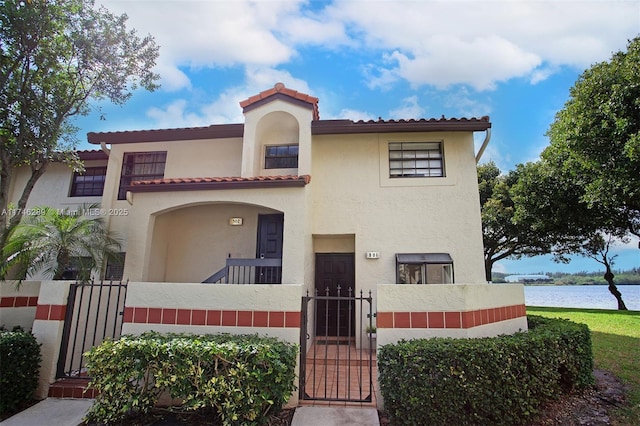 mediterranean / spanish home featuring a fenced front yard, stucco siding, a water view, a gate, and a balcony