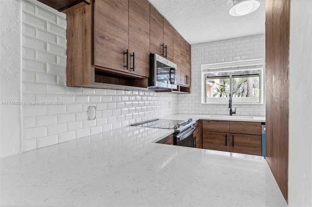 kitchen featuring tasteful backsplash, appliances with stainless steel finishes, brown cabinetry, a sink, and a textured ceiling