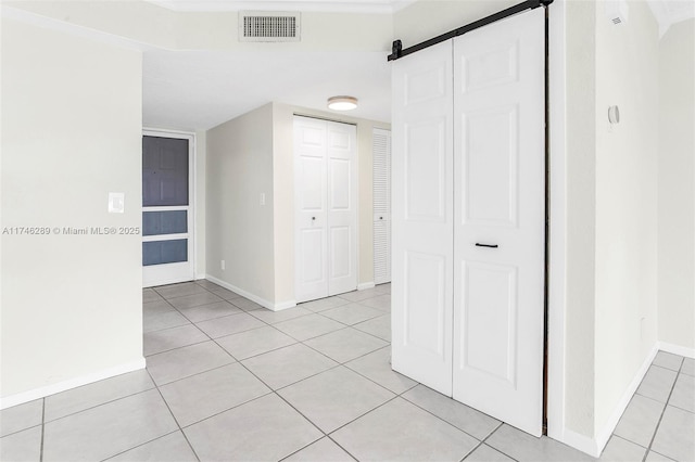 corridor with light tile patterned floors, a barn door, visible vents, and baseboards