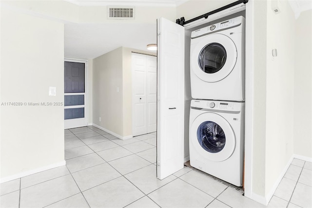 clothes washing area featuring light tile patterned floors, stacked washer and dryer, visible vents, laundry area, and baseboards