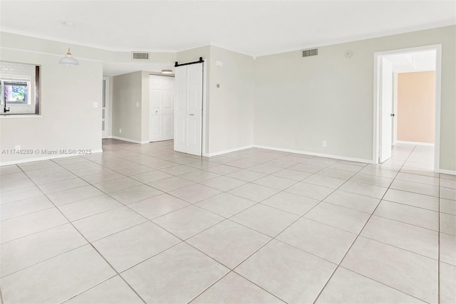 spare room featuring light tile patterned floors, a barn door, visible vents, and baseboards