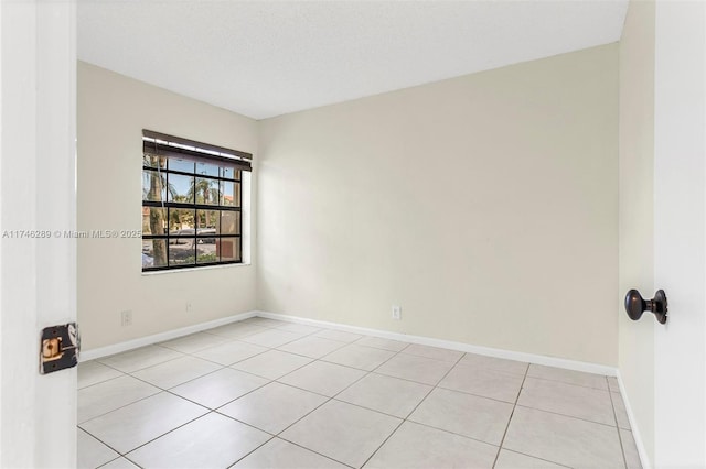 unfurnished room with light tile patterned floors, a textured ceiling, and baseboards