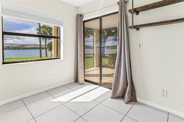 spare room with a water view, baseboards, and light tile patterned flooring