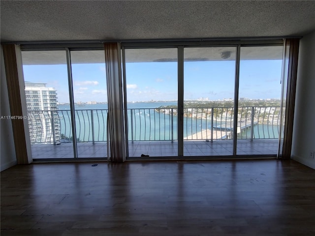 unfurnished room featuring dark wood-type flooring, floor to ceiling windows, a textured ceiling, and a water view