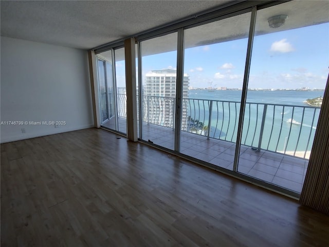 empty room with a water view, dark wood-type flooring, a textured ceiling, and a wall of windows