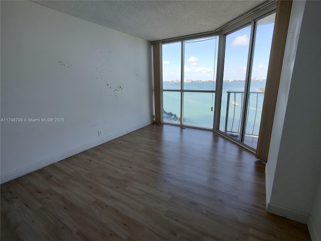 spare room with floor to ceiling windows, a water view, dark hardwood / wood-style floors, and a textured ceiling