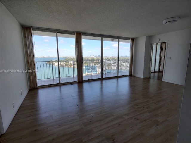 spare room featuring a water view, floor to ceiling windows, dark wood-type flooring, and a textured ceiling