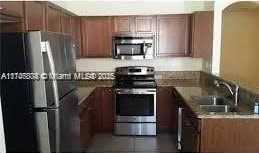 kitchen with sink, stainless steel appliances, dark tile patterned flooring, and stone counters