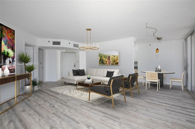 living room with an inviting chandelier, a textured ceiling, and light wood-type flooring