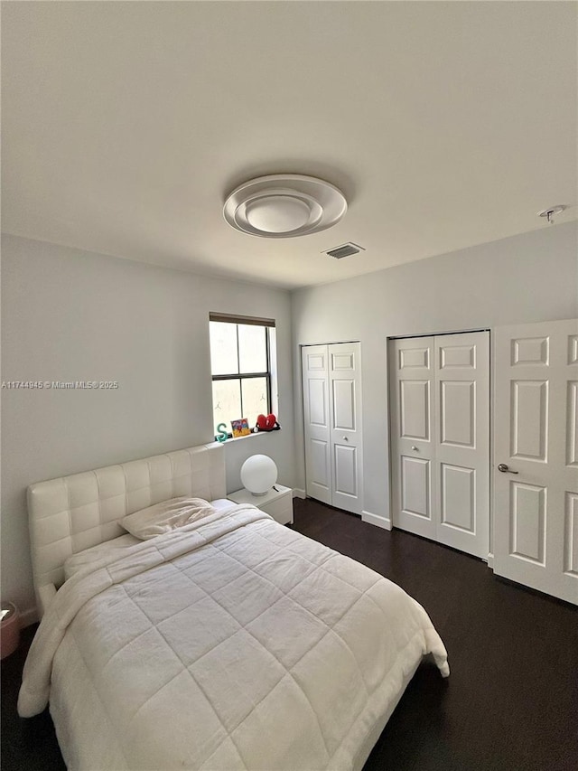 bedroom featuring baseboards, visible vents, and multiple closets