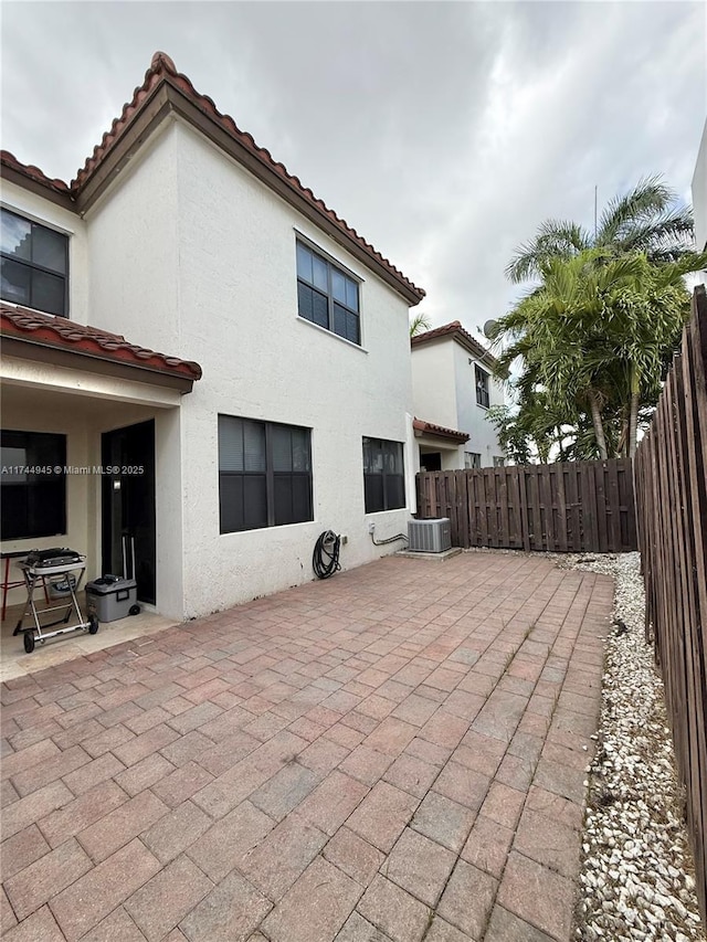 rear view of house with a tile roof, a patio, stucco siding, central AC unit, and a fenced backyard