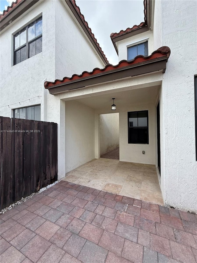 property entrance with stucco siding, a tile roof, fence, and a patio