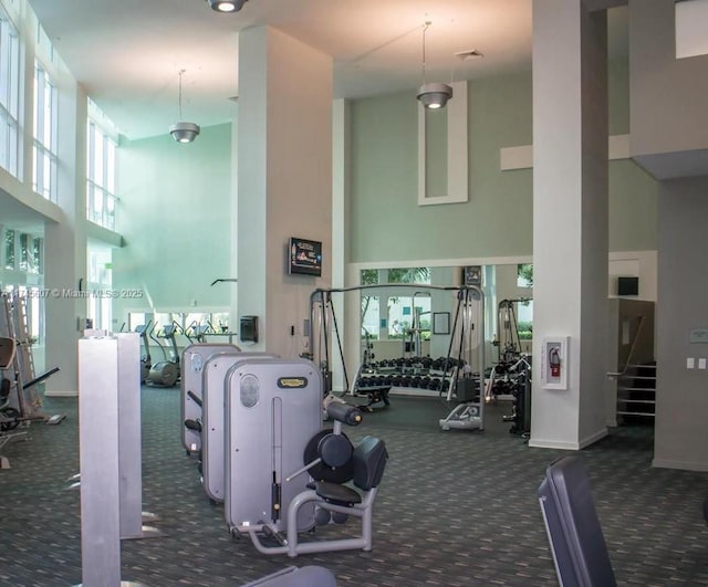 exercise room with a towering ceiling, visible vents, baseboards, and dark colored carpet