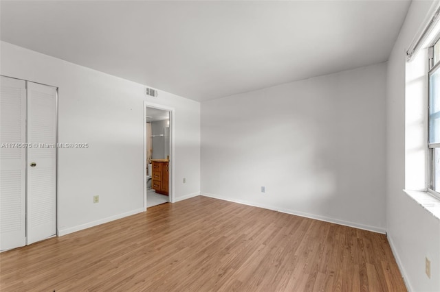 unfurnished bedroom featuring a closet, ensuite bathroom, multiple windows, and light wood-type flooring