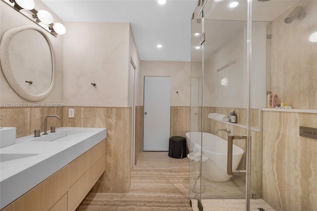 bathroom with tile walls, double vanity, a freestanding bath, a sink, and a shower stall