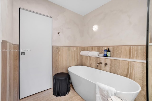 bathroom featuring a freestanding tub, a wainscoted wall, and wood finished floors