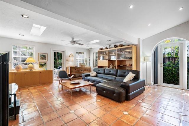 tiled living room featuring a skylight, ceiling fan, and beam ceiling