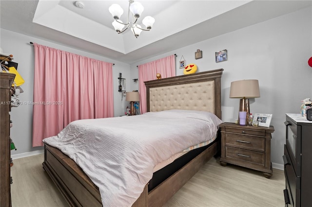 bedroom featuring a chandelier, a tray ceiling, baseboards, and light wood finished floors