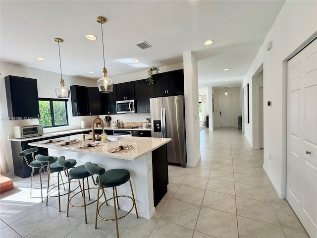 kitchen with appliances with stainless steel finishes, decorative light fixtures, a kitchen breakfast bar, and an island with sink