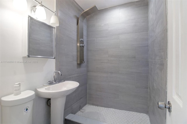 bathroom with tiled shower, toilet, and sink