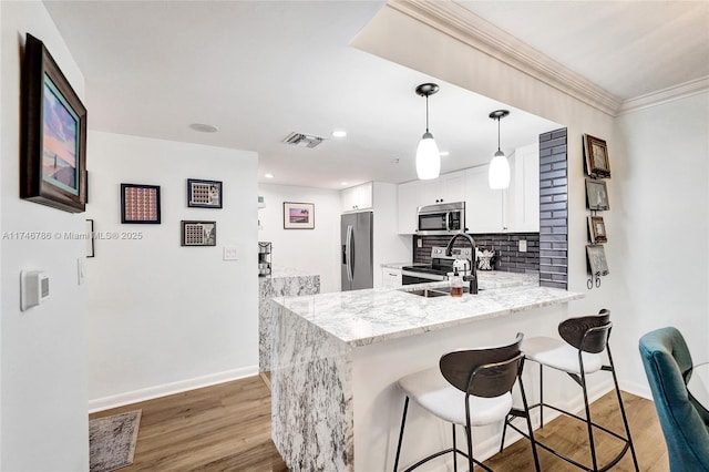 kitchen featuring appliances with stainless steel finishes, decorative light fixtures, white cabinets, kitchen peninsula, and light stone countertops