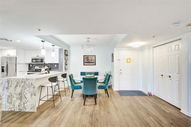 dining room with crown molding, an inviting chandelier, and light wood-type flooring