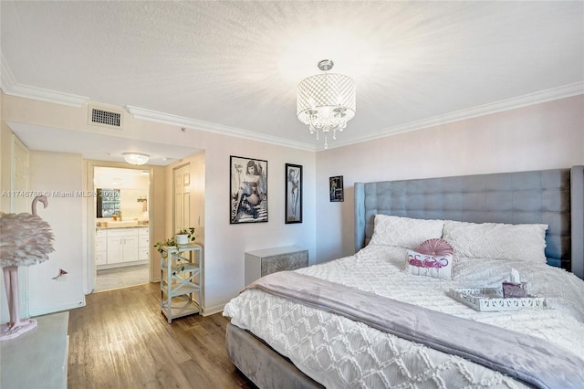 bedroom with connected bathroom, hardwood / wood-style floors, ornamental molding, and a chandelier