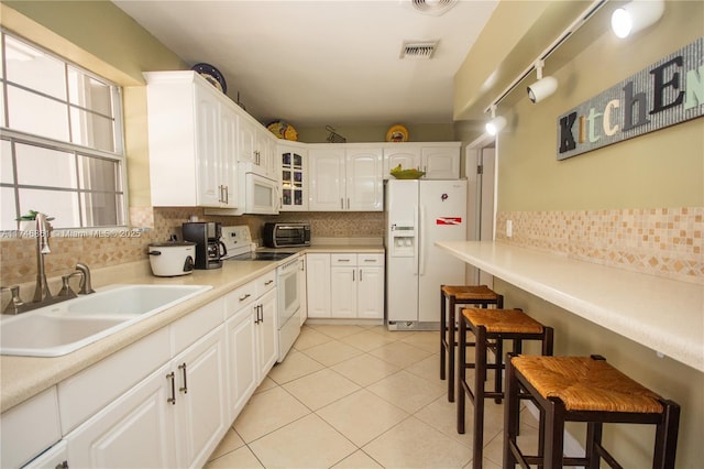 kitchen featuring light tile patterned floors, white appliances, a sink, a kitchen bar, and glass insert cabinets