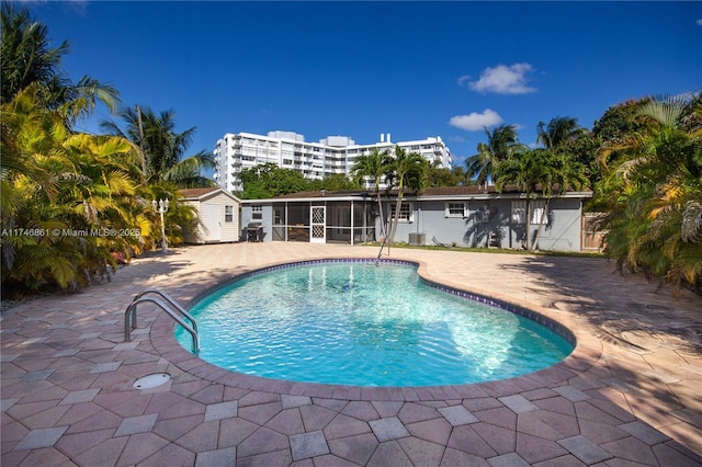 outdoor pool featuring a sunroom, a patio, and an outdoor structure