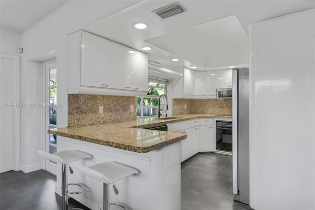 kitchen featuring white cabinetry, a kitchen bar, kitchen peninsula, and light stone countertops