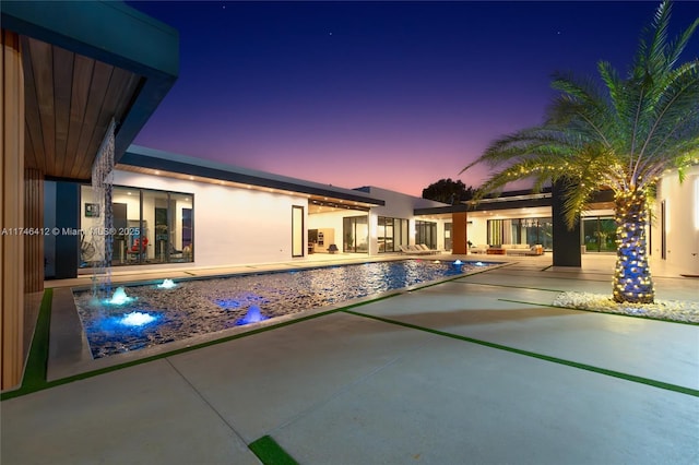 pool at dusk featuring a patio and pool water feature