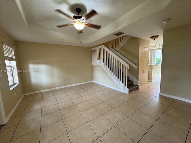 tiled empty room featuring ceiling fan, a textured ceiling, and a tray ceiling