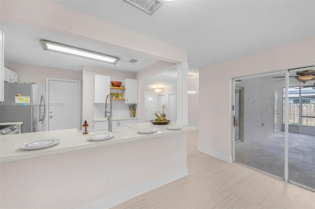 kitchen with stainless steel refrigerator, sink, light stone counters, and white cabinets