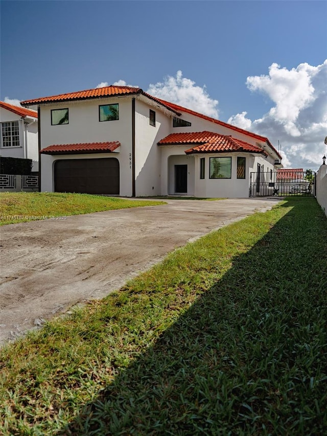 rear view of house with driveway, a lawn, a tiled roof, fence, and stucco siding